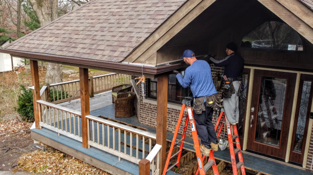 Two Gutter Pros installers working from ladders on a home porch roof