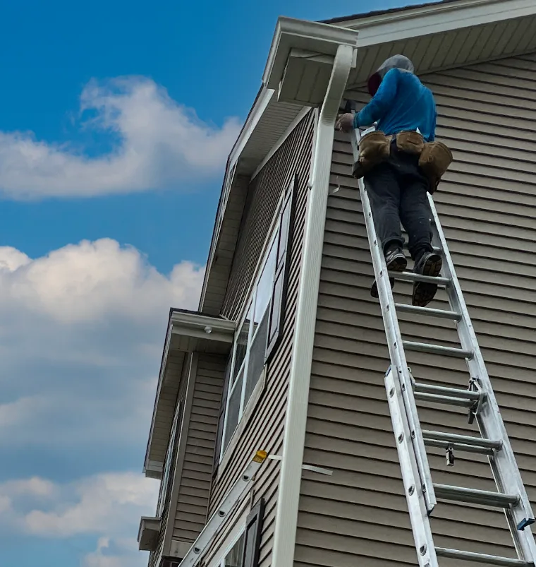 Gutter Pros technician carrying materials up a ladder to the roofline